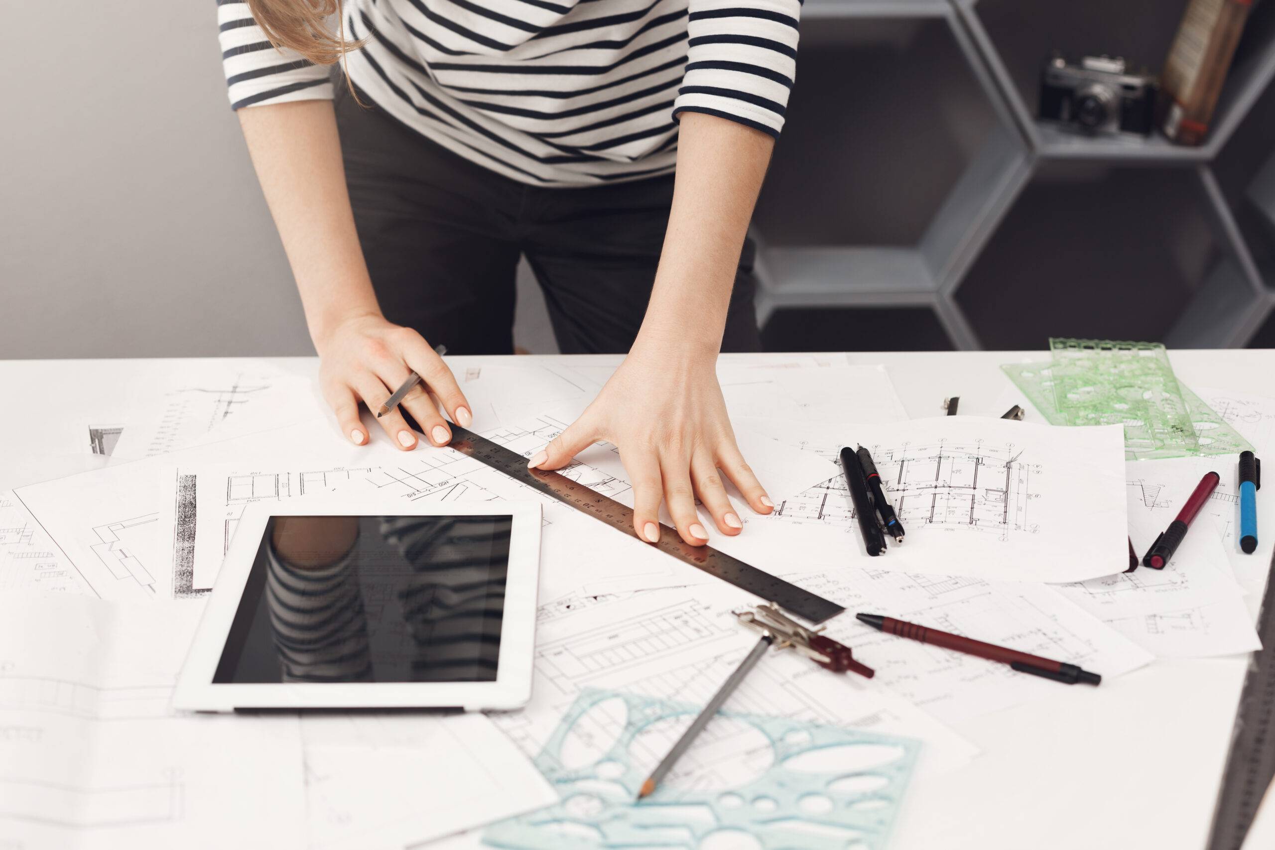  top-view-young-good-looking-architect-student-girl-casual-striped-shirt-black-jeans-standing-near-table-holding-ruler-pen-hands-making-drawings-watching-movie-digital-table-gett.jpg